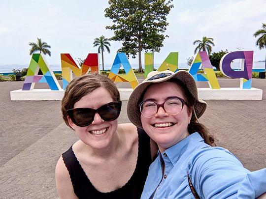 two women, smiling, in front of Panama sign